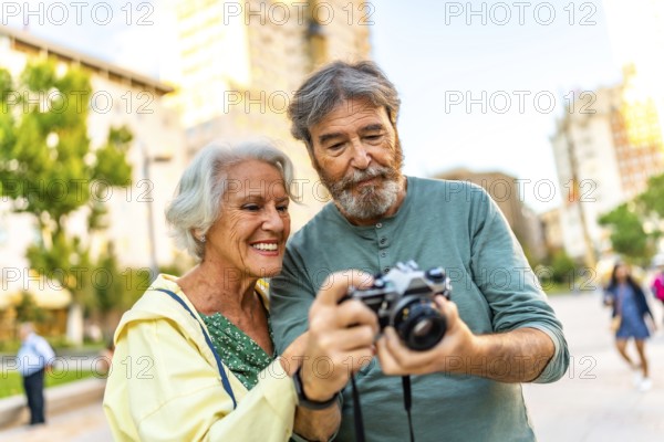Senior modern caucasian couple looking at the images on a camera screen while visiting a city