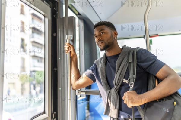 African casual businessman standing on a public bus looking through the window in the city