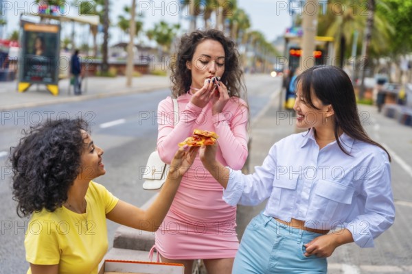 Multi-ethnic female friends sharing a delicious pizza eating in the street