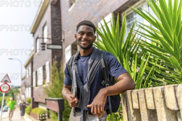 Portrait of a confident african entrepreneur holding laptop standing next to a house in a residential district