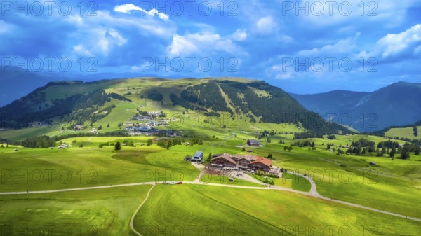 Stunning aerial view capturing green meadows, traditional houses, and rolling hills beneath a vibrant blue sky in alpe di siusi, dolomites