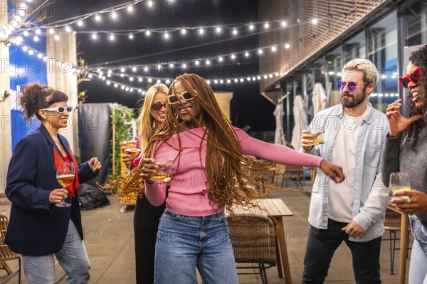 Happy modern african woman with long braided hair dancing with multi-ethnic friends at night party outdoors in the terrace of a bar