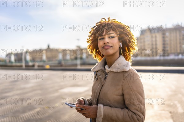 Happy beauty latin young using phone and listening to music standing in the city during sunset