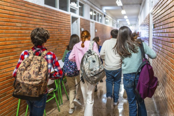 Group of students walking down school hallway between classes, carrying backpacks and rushing to their next lesson