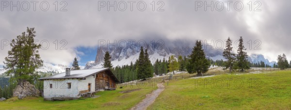 Panoramic view of the partly cloudy Geißler group with a hiking trail and a hut of the Glatsch Alm in the foreground