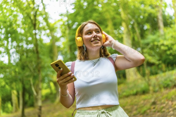 Caucasian young woman listening to music smiling looking up while standing in a footpath in the forest