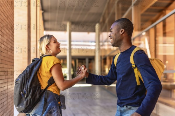 Side view of two happy multi-ethnic students shaking hands at the university