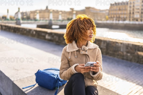Latin beauty woman using phone sitting in the city next to the river
