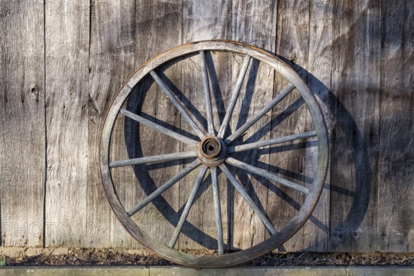 Old wagon wheel leaning against a barn wall, Düstermühle, Legden, district of Wehr, Münsterland, North Rhine-Westphalia, Germany, Europe