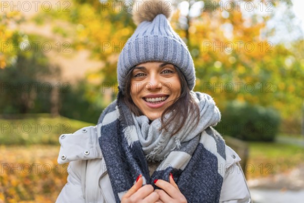 Portrait of a confident smiling woman with woolly hat and scarf in a park
