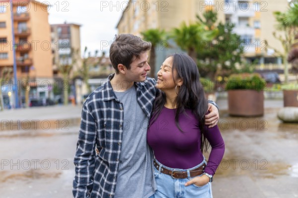 Happy multiethnic couple shares a joyful moment outdoors, embracing and smiling at each other, surrounded by an urban setting with greenery