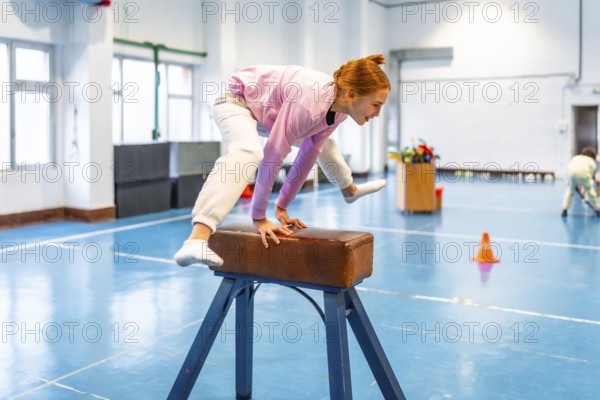 Redhead student practicing gymnastics on pommel horse, showing balance and coordination in school gym class