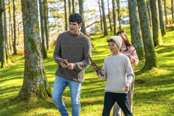 Caucasian father and two children collecting wood for camp fire while trekking in the forest