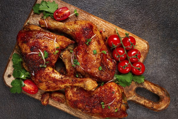 Grilled fried chicken legs, served with fresh cherry tomatoes, and herbs, on a wooden chopping board, homemade, no people