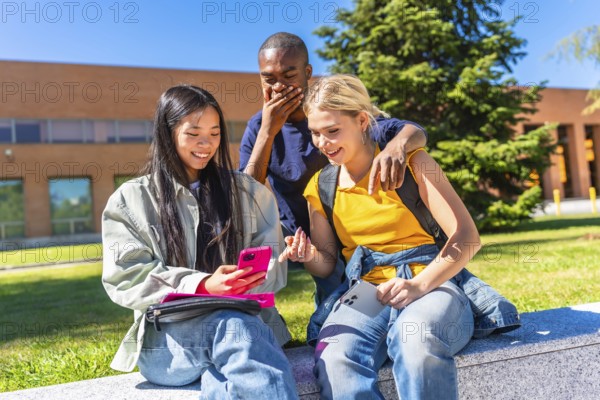 Multiracial group of students using mobile and expressing surprise sitting in the campus