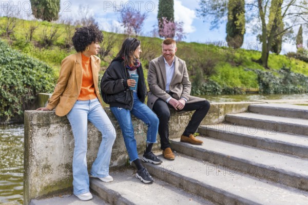 Three young professionals enjoying a break, chatting and laughing together by a canal in a city park