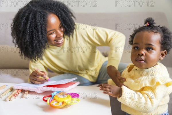 Adorable child and african mother drawing at home sitting on the sofa in the living room