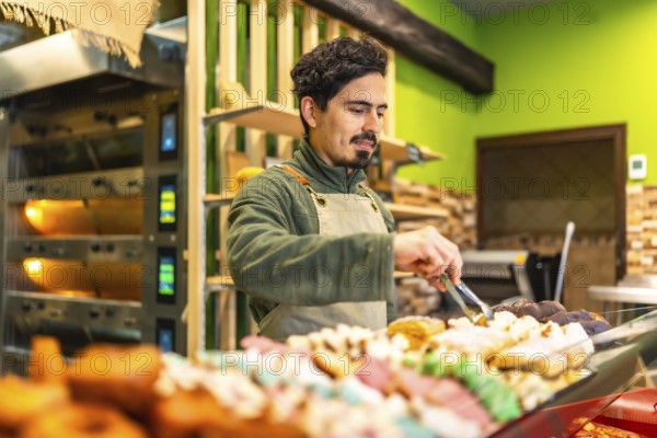 Latin young male baker arranging pastries on the counter of an artisan bakery shop