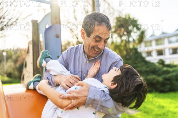 Grandfather holding his grandson and playing together at the playground, having a joyful and playful moment