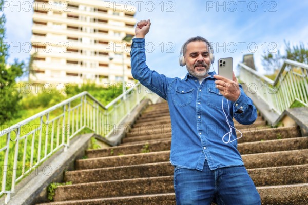Mature man dancing while listening to music with phone in an urban stairs in the city
