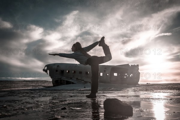 Woman on the Solheimasandur plane in Iceland performing a Natarajasana yoga pose to open the hip and heart