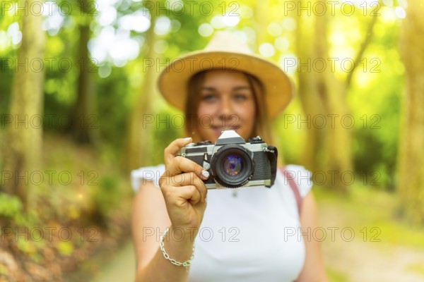 Portrait with selective focus on the camera in hands of a young female caucasian photographer in the forest