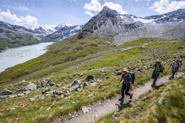 Three mountaineers on a hiking trail at a blue mountain lake, reservoir Lac des Dix, behind mountain peak Mont Blanc de Cheilon, Hérménence, Valais Alps, Valais, Switzerland, Europe