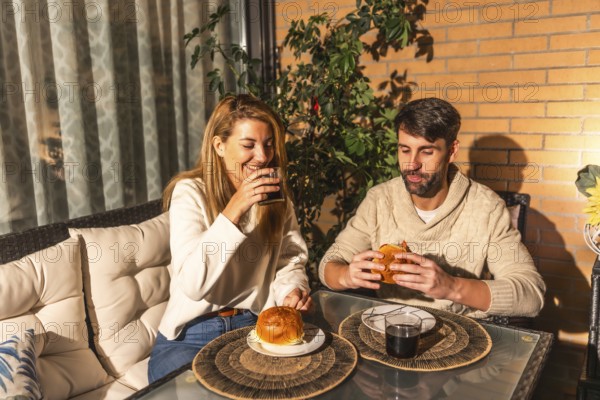 Smiling man and woman enjoying burgers and beverages on a cozy terrace, creating a warm and inviting atmosphere