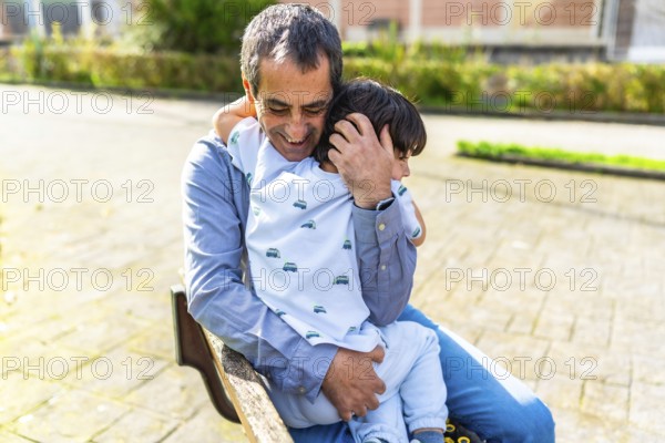 Grandfather hugging grandson while sitting on a park bench, enjoying a tender moment together