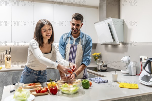 Young couple smiling and joyfully preparing a vibrant, healthy salad together in their modern kitchen, sharing moments of love and teamwork