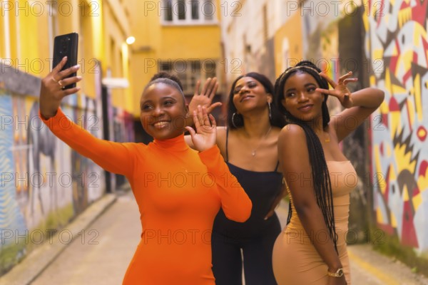 San Sebastián, Gipuzkoa Spain, February 2021: Three girls taking a selfie. Fashionable urban style with three black African girls on a city street, tight dresses. Girlfriends lifestyle