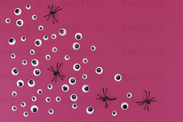 Halloween flat lay with lots of spooky googly eyes and plastic spiders on pink background with empty copy space