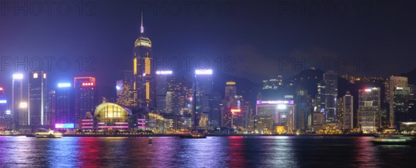 Panorama of Hong Kong skyline cityscape downtown skyscrapers over Victoria Harbour in the evening illuminated tourist boats and ferries, Hong Kong, China, Asia