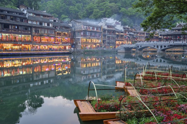 Chinese tourist attraction destination, Feng Huang Ancient Town (Phoenix Ancient Town) on Tuo Jiang River with bridge illuminated at night. Hunan Province, China, Asia
