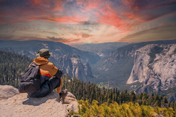A young man on the trek sitting on the Sentinel Dome lookout in Yosemite National Park looking at El Capitan Mountain. United States