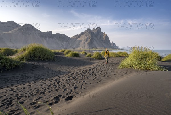 Tourist on a sand dune, Black beach with volcanic sand, Sand beach, Dunes with grass, Stokksnes headland, Klifatindur mountain range, Austurland, East Iceland, Iceland, Europe