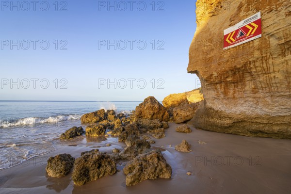 ROCKFALL UNSTABLE CLIFFS, KEEP A SAFE DISTANCE is written in English on a warning sign in Portugal on the cliffs of the Atlantic Ocean. Rocks and stones break out here again and again and injure people., Albufeira, Faro, Portugal, Europe
