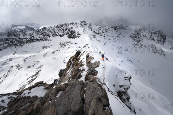 Mountaineer descending the narrow ridge of Piz Laviner, view of mountain panorama in wintry mountain landscape with dramatic clouds, Grisons Haute Route, Albula Alps, Rhaetian Alps, Grisons, Eastern Switzerland, Switzerland, Europe