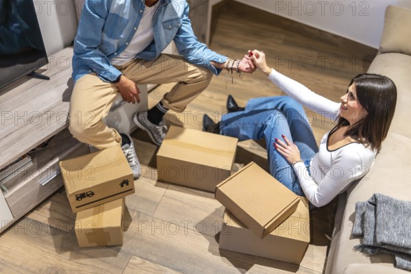 Happy couple holding hands and taking a break from unpacking cardboard boxes in their new home