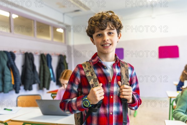 Portrait of a smiling preteen student wearing backpack in a classroom with classmates studying on background
