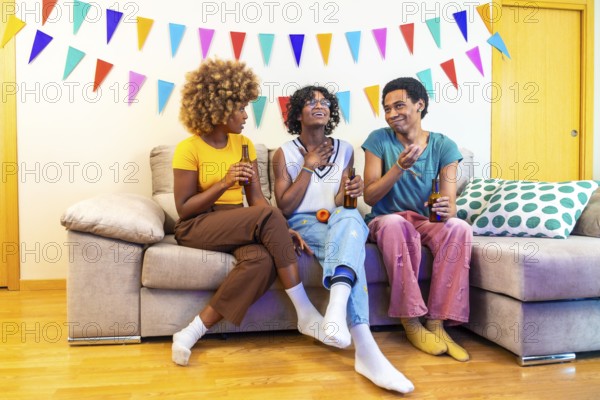 Multi-ethnic friends chatting during party at home sitting on the sofa with beers and karaoke microphone