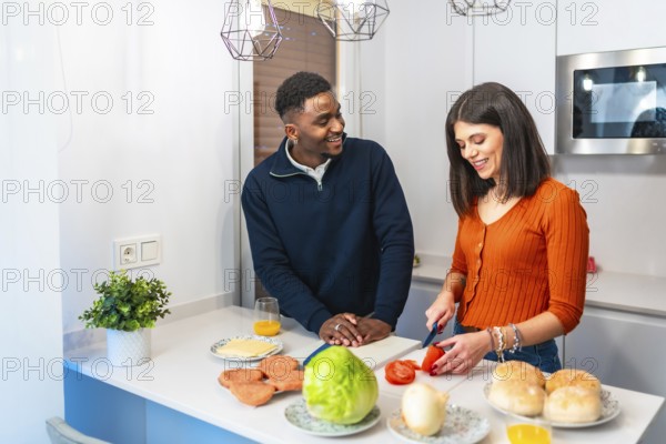 Young multiethnic couple smiling and joyfully preparing delicious burgers together in their modern kitchen, sharing love and laughter