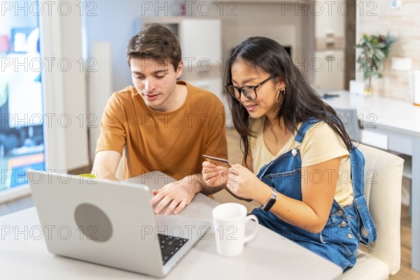Multiethnic couple using a laptop and a credit card, making online purchases together in their modern apartment