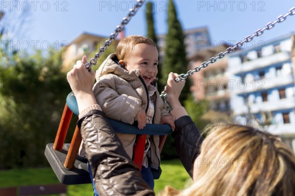 Happy little boy enjoying time on a swing while his mother lovingly pushes him in a vibrant playground, filled with laughter and joy