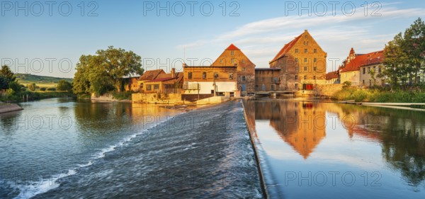 Historic watermill reflected in the river Unstrut with weir in the evening light, Laucha, Saxony-Anhalt, Germany, Europe