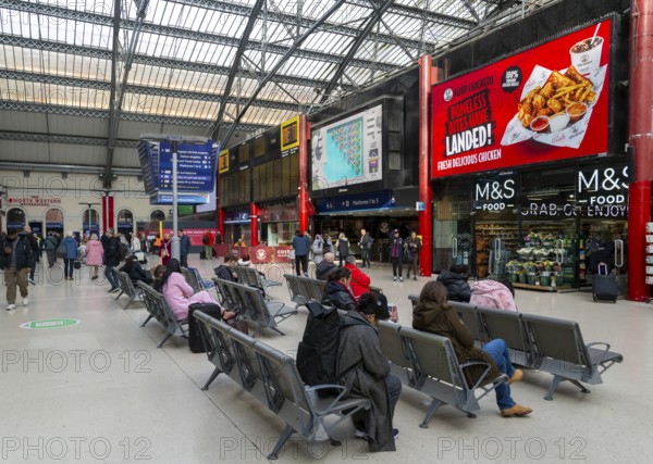 People sitting in seats in concourse area of Lime Street railway station, Liverpool, England, UK