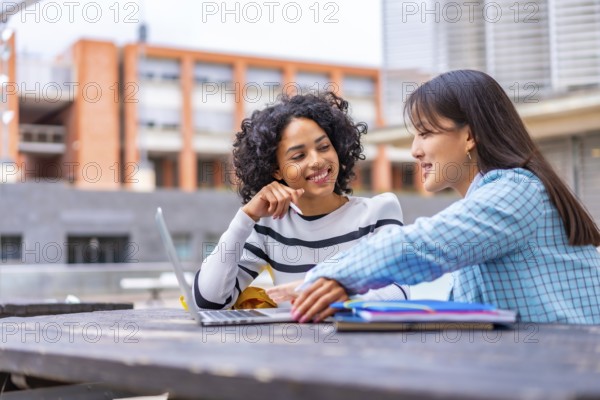 Side view of two multiracial woman studying together using laptop in the university campus