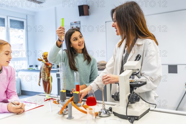 Female teacher assisting students during a chemistry experiment in a school laboratory, promoting stem education and scientific exploration