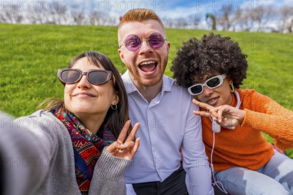 Three happy multi ethnic friends are taking a selfie while making the peace sign, enjoying a sunny day in a green park
