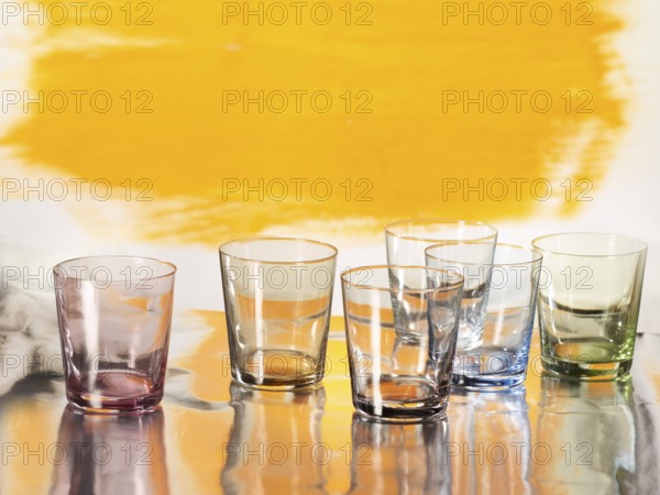 Various glasses on silver foil, yellow coloured surface behind, studio shot
